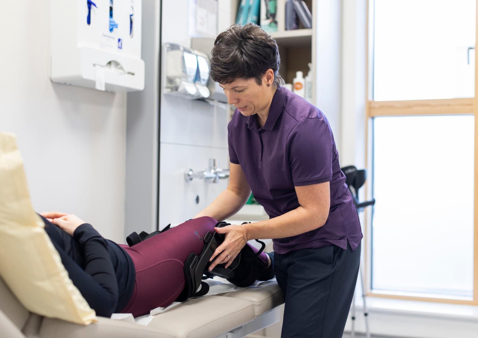 Amanda Marsh fitting an Ossur knee brace to a patient lying on a treatment bed