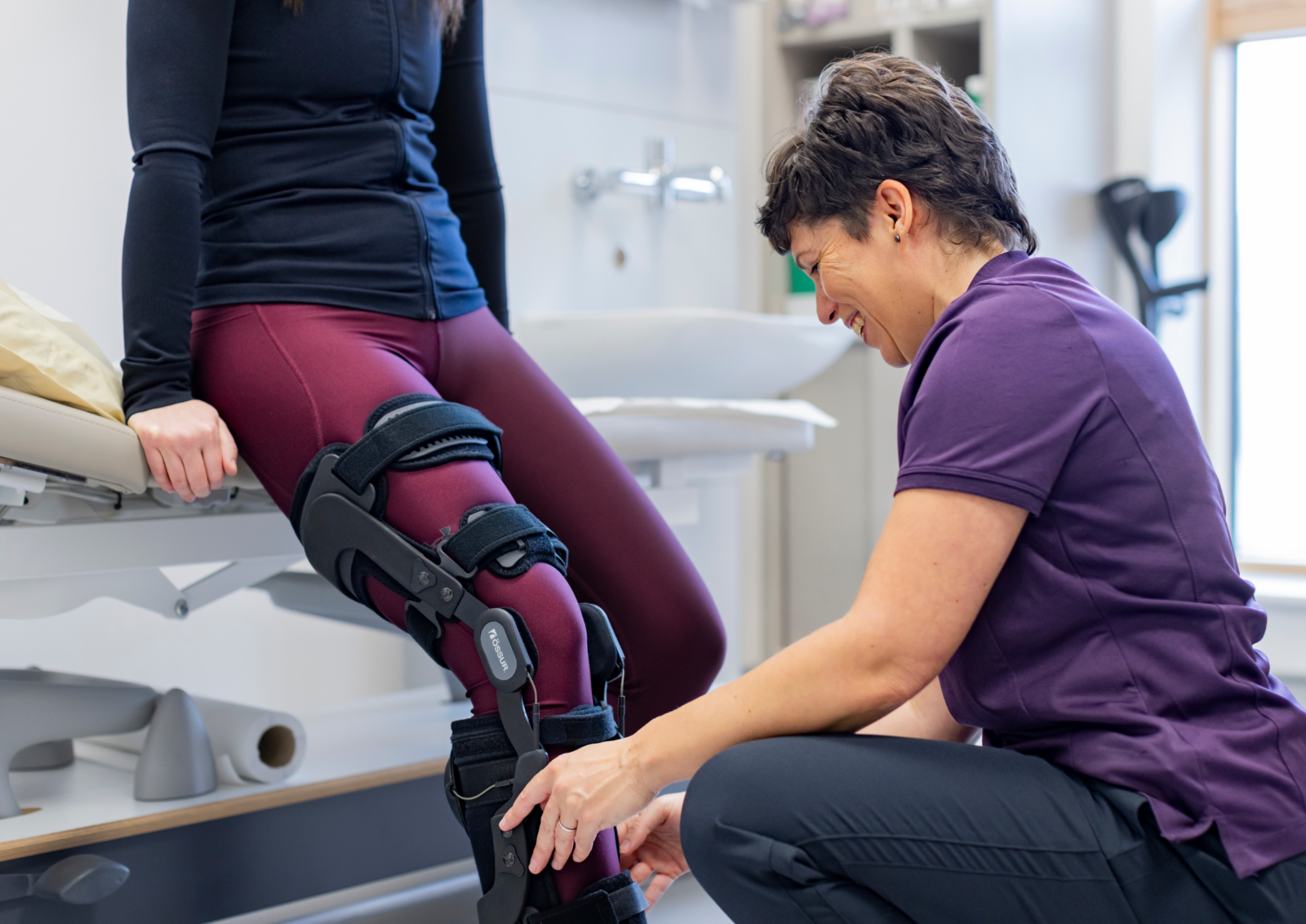Amanda Marsh fitting an Ossur knee brace to a patient sitting on the edge of a treatment bed