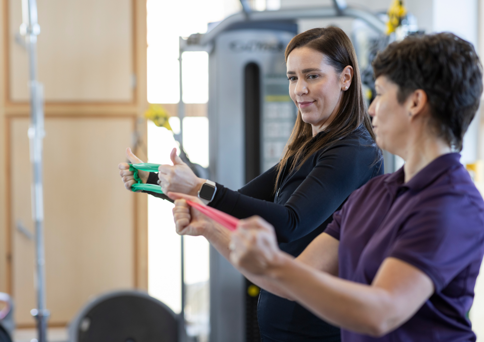 Amanda Marsh demonstrating resistance band exercises to a smiling a patient who is watching and copying